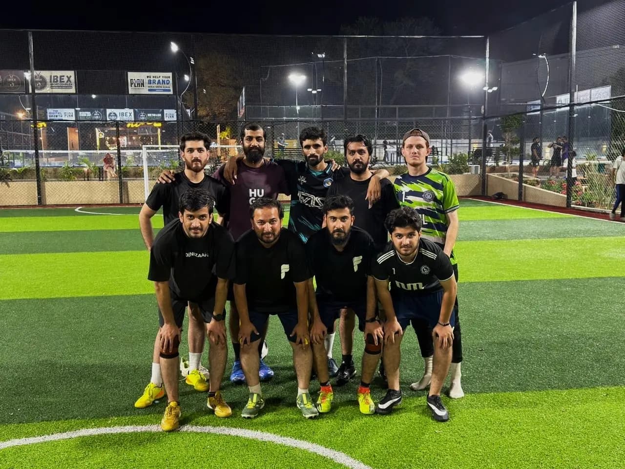 The team's football side posing together on a floodlit five-a-side pitch at night